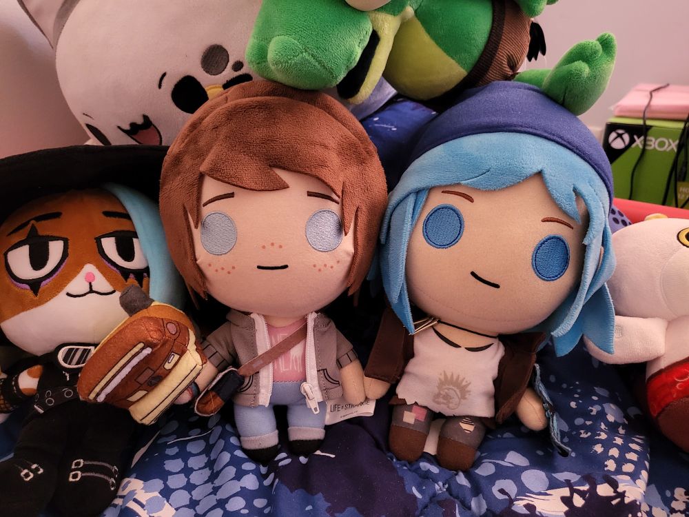 Max & Chloe plushies from Life is Strange game.
They're holding hands
A bunlith plushie is near them, a lil gator game one too and cat plushies as well