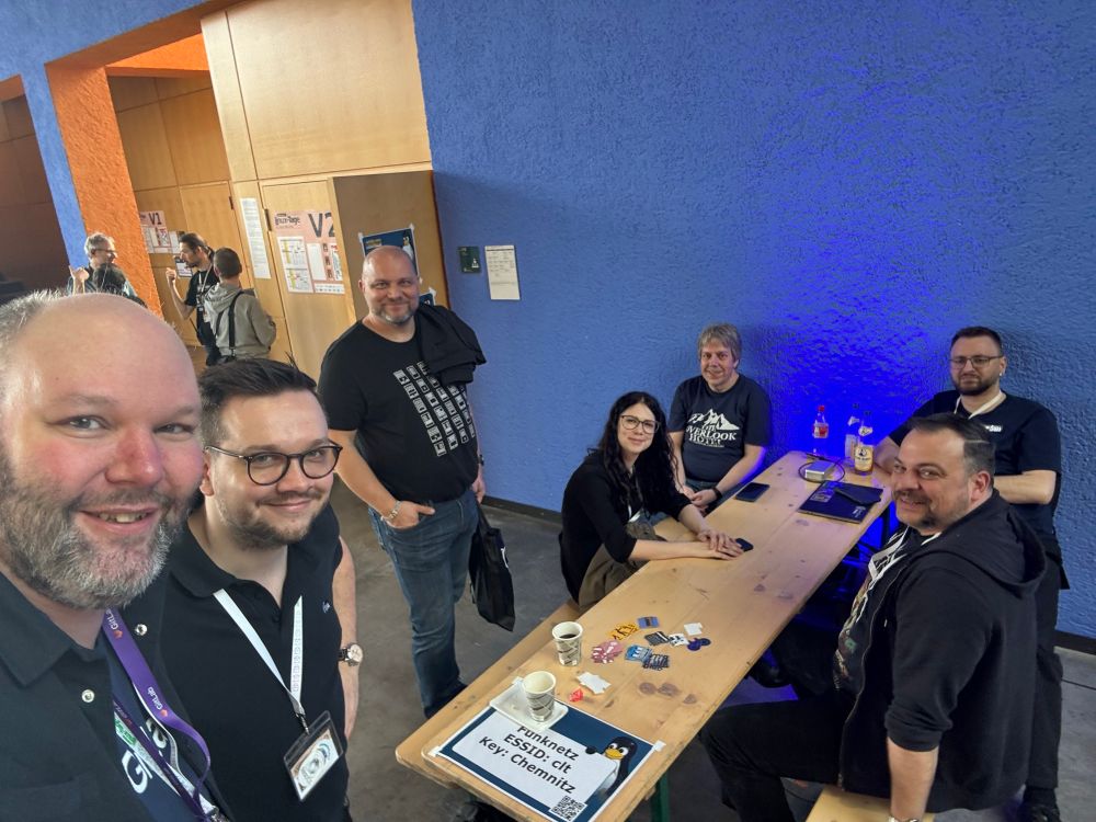 7 folks standing/sitting, connected together at the event, in front of one of the student lecture rooms at TU Chemnitz. 