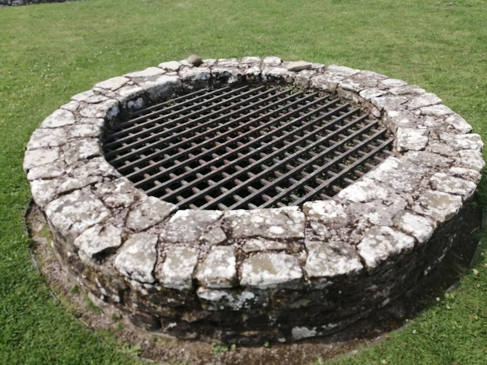 A stone surrounded well, covered with an iron grill.