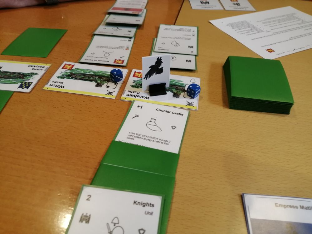 Overlapping cards representing castles, armies, etc, as well as some dice and a stand-up token with a flying raven drawn on it