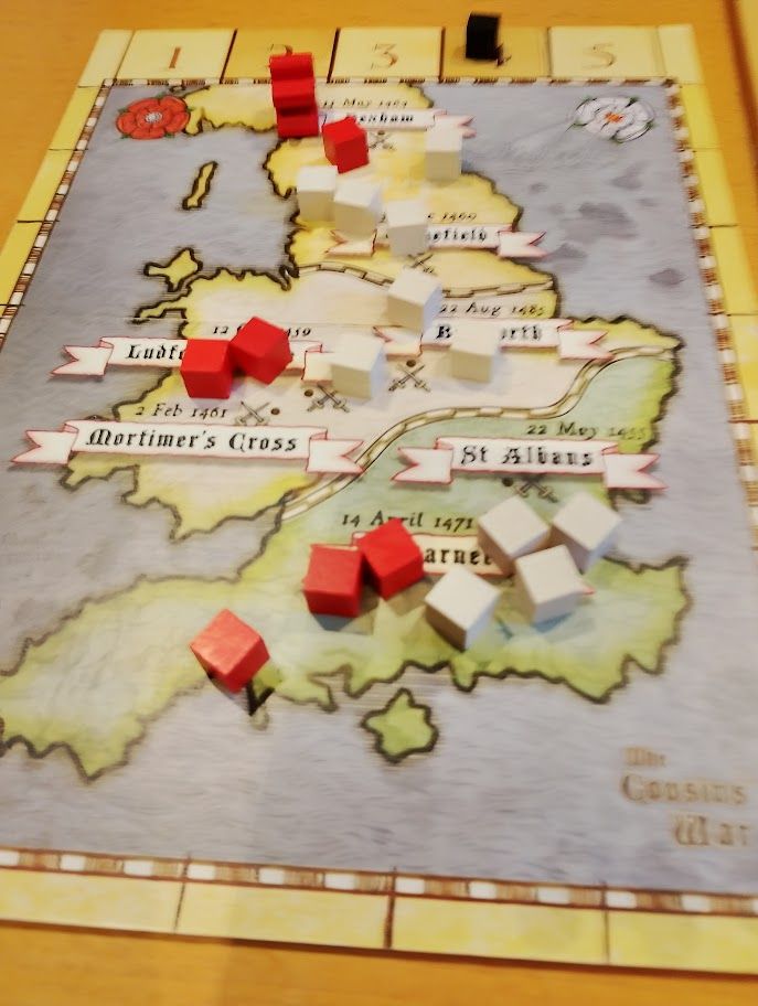 A small game board, depicting a stylised map, largely of England and Wales, on which are red and white cubes.