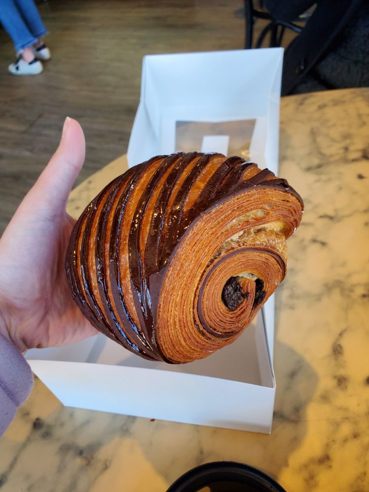 A large "chocolate croissant" with a glossy striped chocolate pattern on top held in hand.