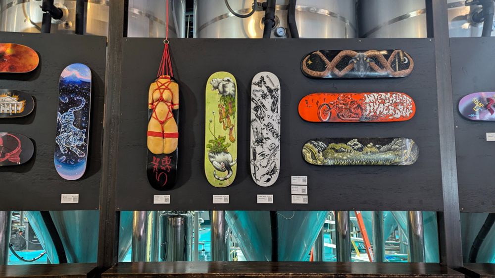 Photograph of a black display board with a variety of colorful artworks created on or out of skateboards hung all over it.