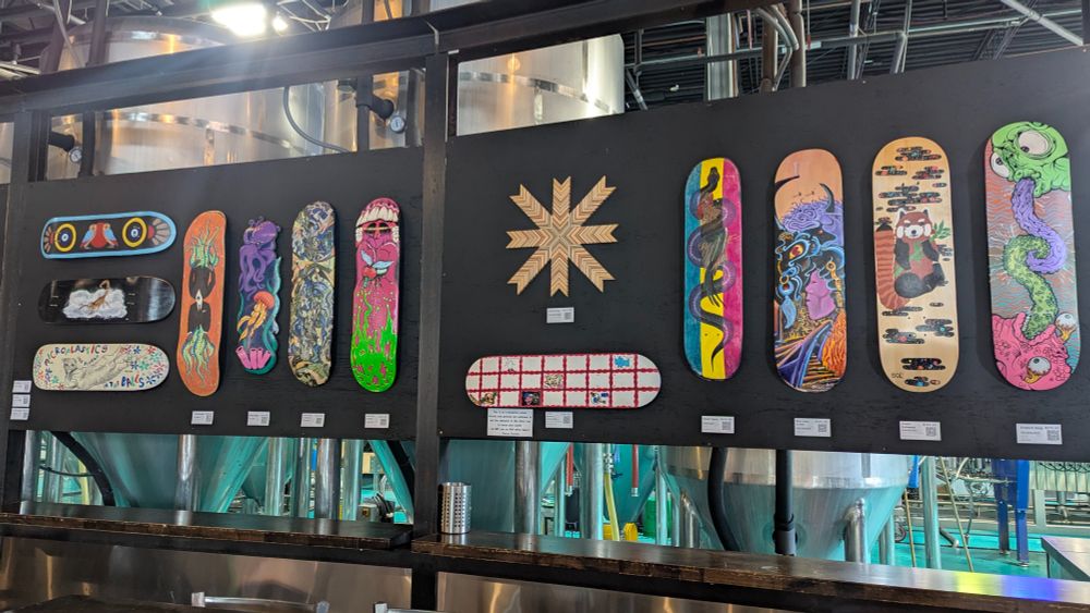 Photograph of a black display board with a variety of colorful artworks created on or out of skateboards hung all over it.
