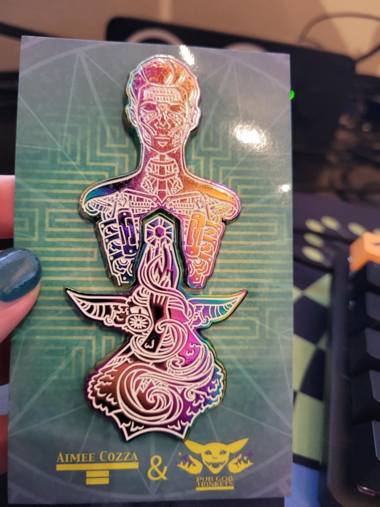 Two anodized pins that fit one into another. They are of a robot head and torso and a goblin handing up a gem to the center core of the robot.