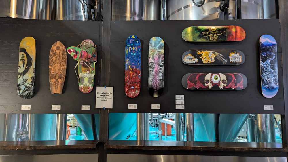 Photograph of a black display board with a variety of colorful artworks created on or out of skateboards hung all over it.