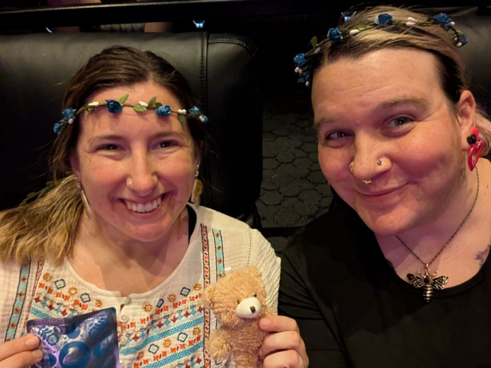 Erica and Mae wearing flower crowns and smiling. Erica is holding the small bear keychain and teabag that came with our tickets
