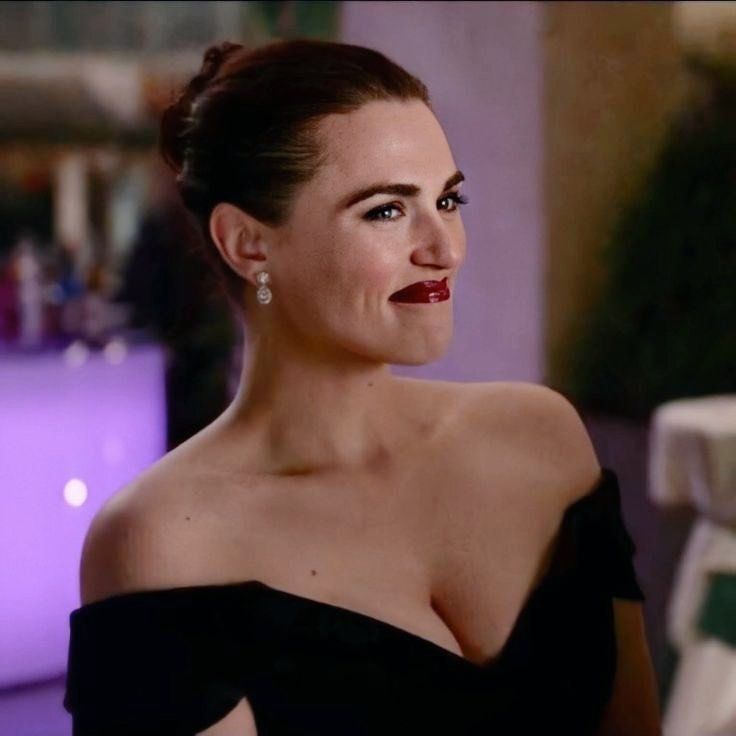 Katie McGrath as Lena luthor in a low cut black dress, grinning at the person stood in front of her 