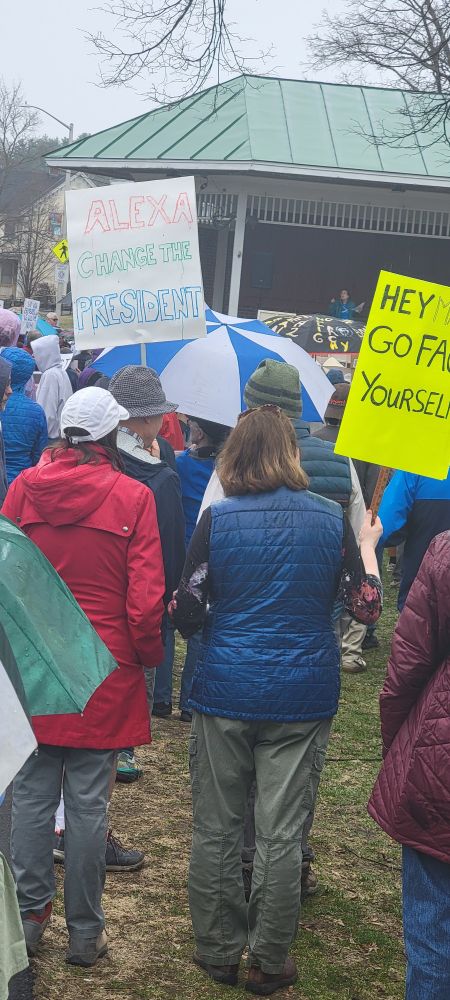 A group of people listening to a speaker at the No Kings! rally in Lebanon, NH on April 19, 2025. A sign reads "Alexa change president."
