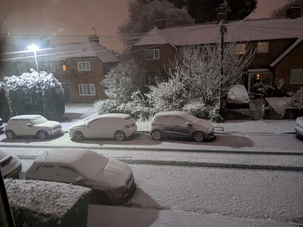 Photo shows a street in the early morning with the cars and road covered in snow.