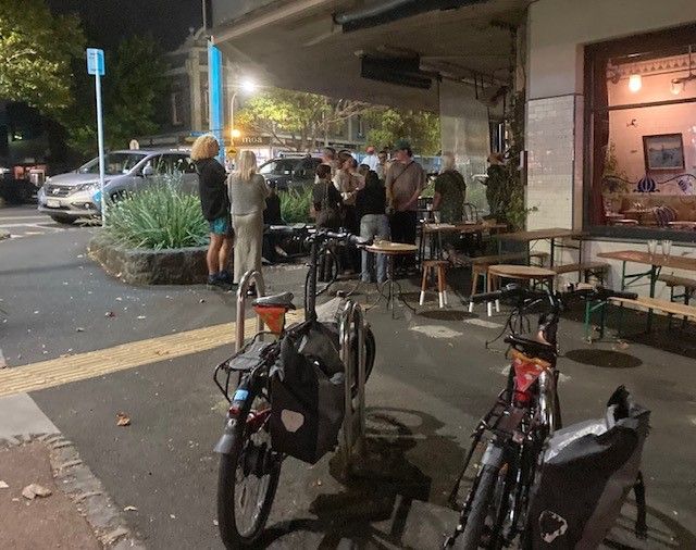 Nighttime, 2 e-bikes parked outside local bar/venue, patrons milling around