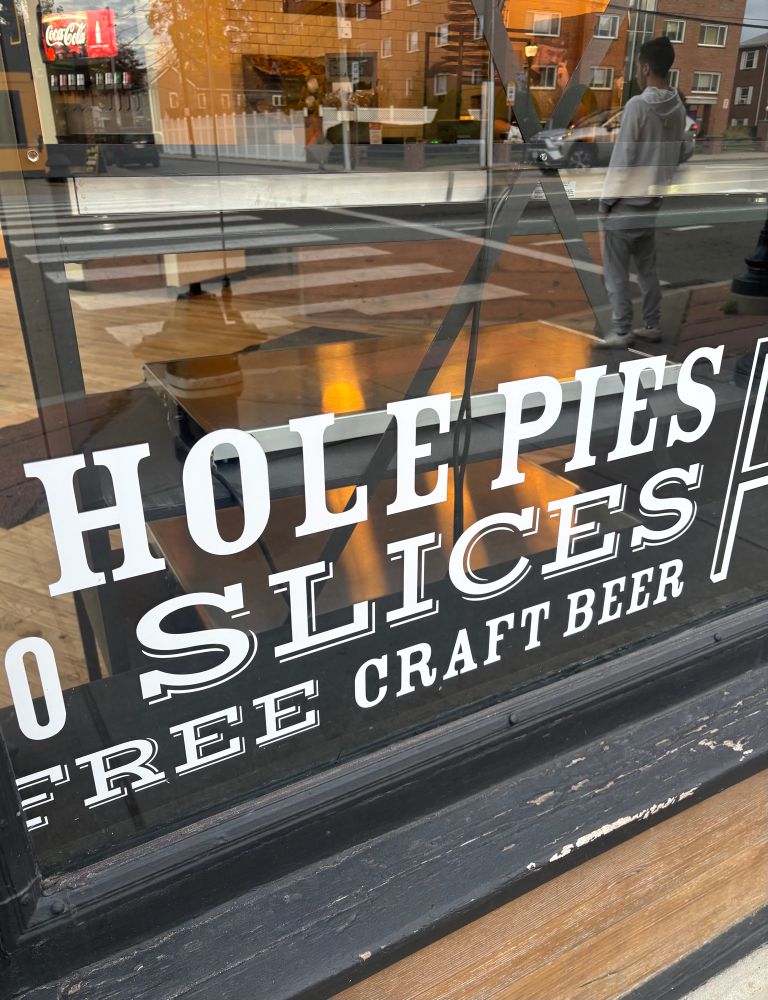 pizza place window with text on it that reads “whole pies” but the W is cut off so it says “hole pies”