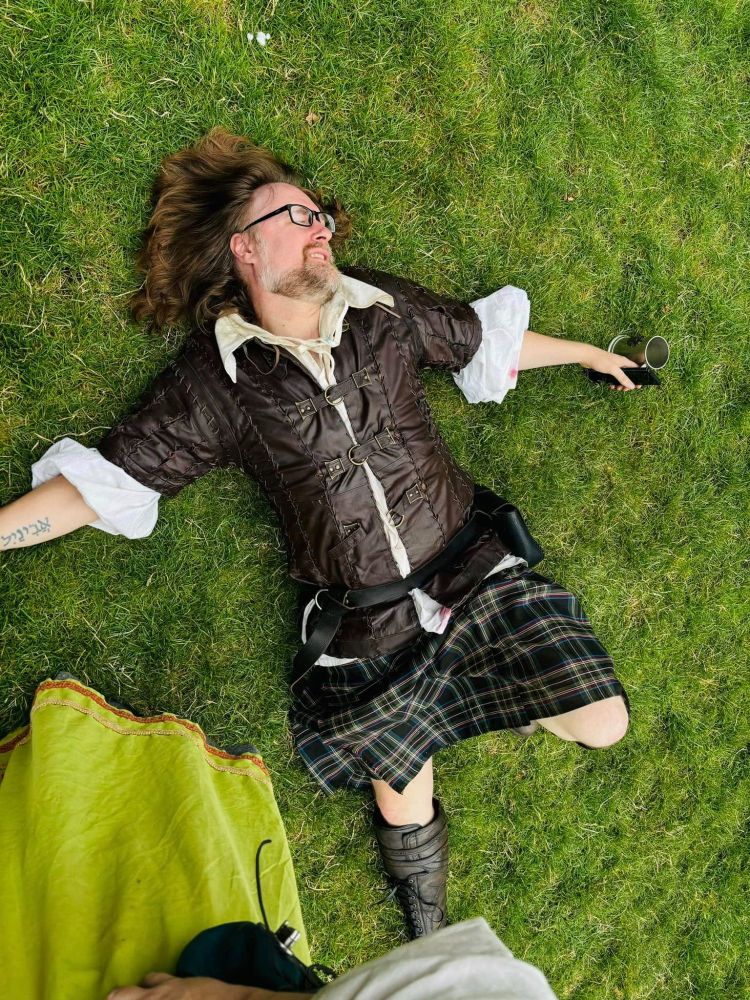 A man in Renaissance Faire garb lies sprawled in the grass. 