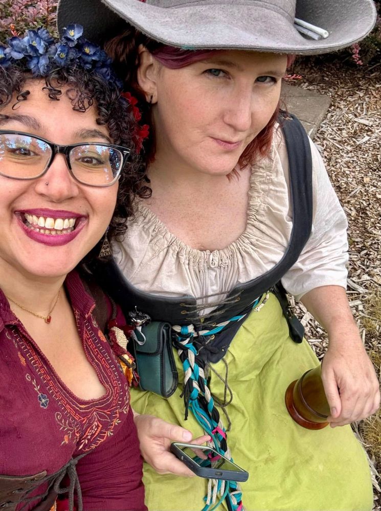 Two women in Renaissance Faire garb pose for the camera from a high angle.  