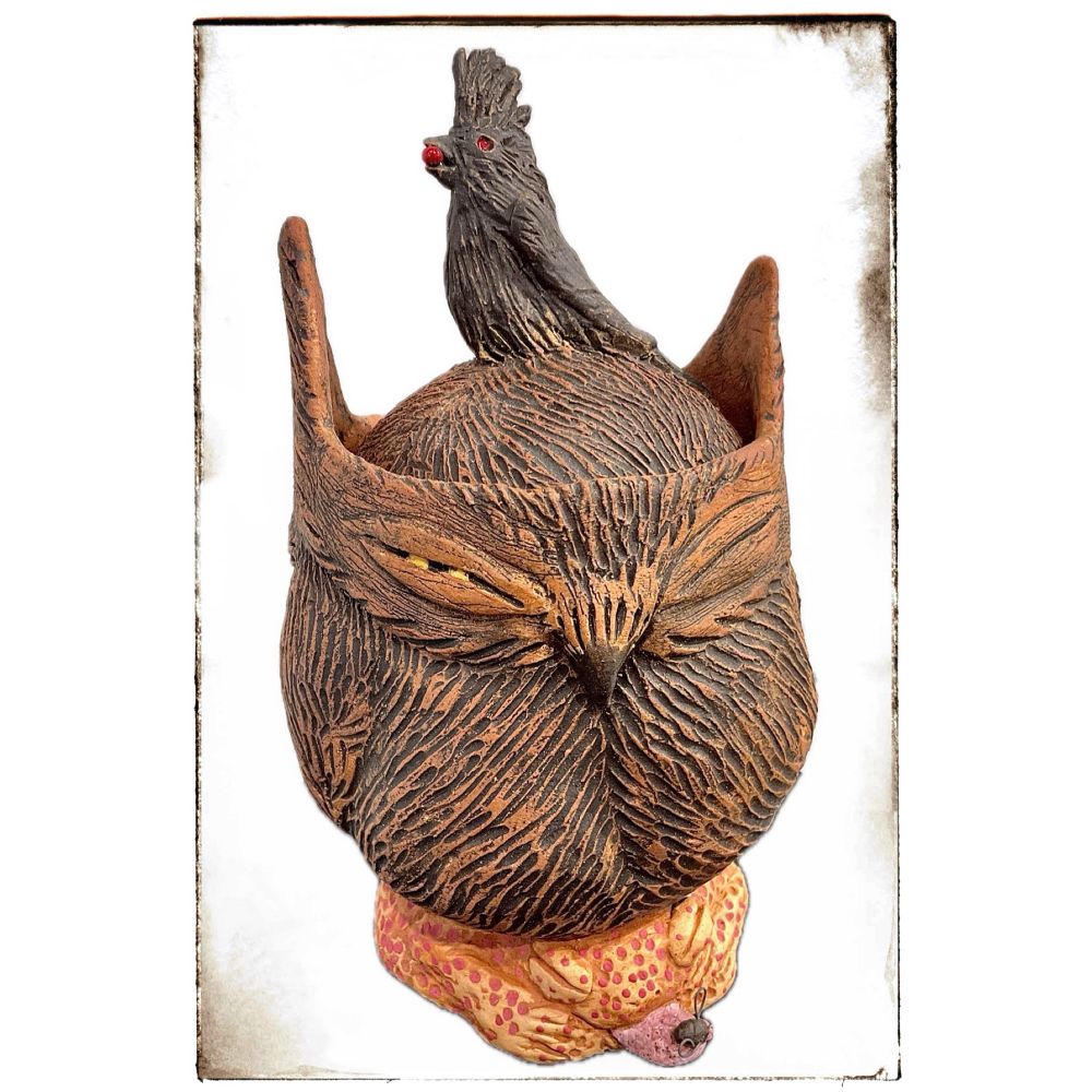Artwork shown: hand built brown, textured clay jar of a cranky-looking owl with one yellow eye open, sitting on a red-spotted toad with a black fly on its tongue, and a crested, black bird on the top of its head, which is the lid of the jar. The bird has a red berry in its beak, and is the knob of the lid.
