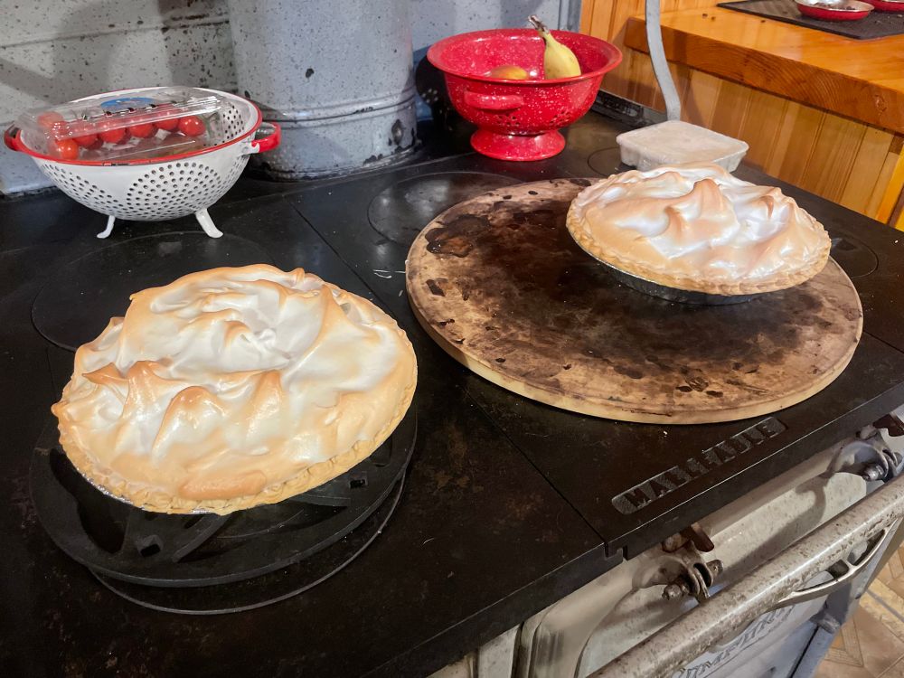 Two lemon meringue pies on a black stove top