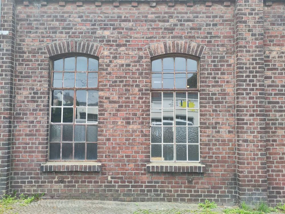 die alte Front eines Fabrikgebäudes aus gebranten Ziegelsteinen. in die Mauer sind Fenster eingelassen die Fenster sind in einen Rahmen zu vier x sechs kleinen Scheiben aufgeteilt. ca 1x 2 Meter hoch. das Material der Rahmen ist sehr verrostet