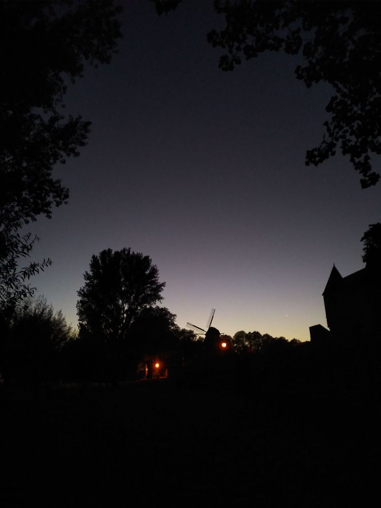 die Sonne zeigt einen silbernen Streifen am Horizont.
davor die nur zu erahnende Stadtmauer. 
aus ihr ragt die Mühle heraus. 
ein Licht leuchtet noch an einem Eingang.
und ein paar Bäume stehen beschaulich in der Gegend rum