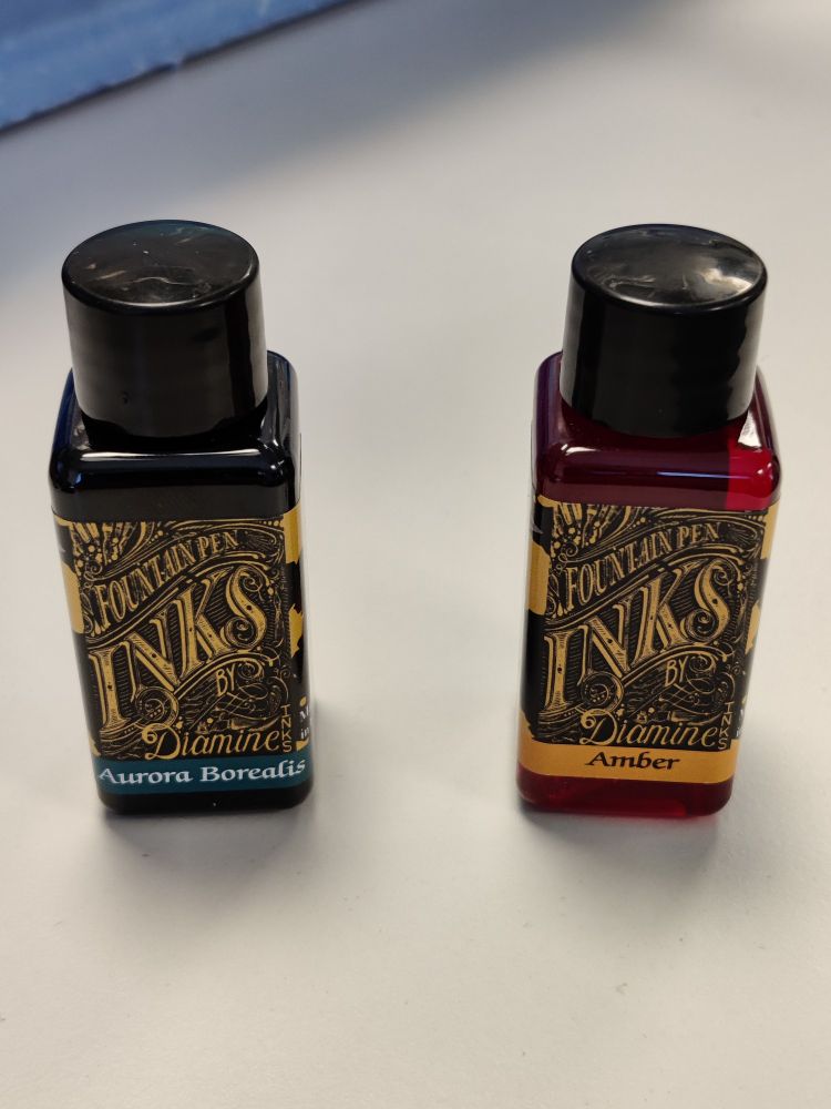 Bottles of Diamine's Aurora Borealis and Amber inks on a light grey tabletop
