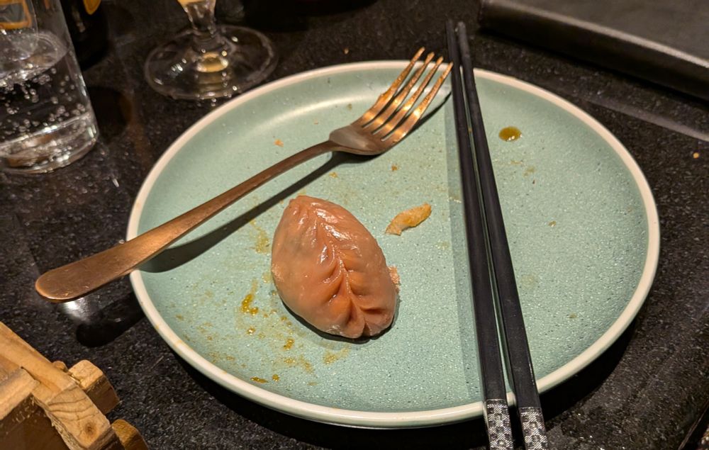 A pinkish-grey dumpling on a blue plate. The dumpling is wet and shiny, and has a puckered seam across the back — y'know, like a dumpling — making it look particularly yonic.