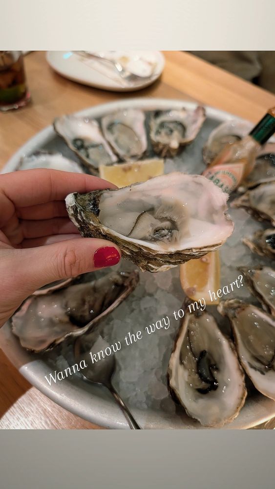 A hand with red nail polish holding an open oyster over a plate of open oysters