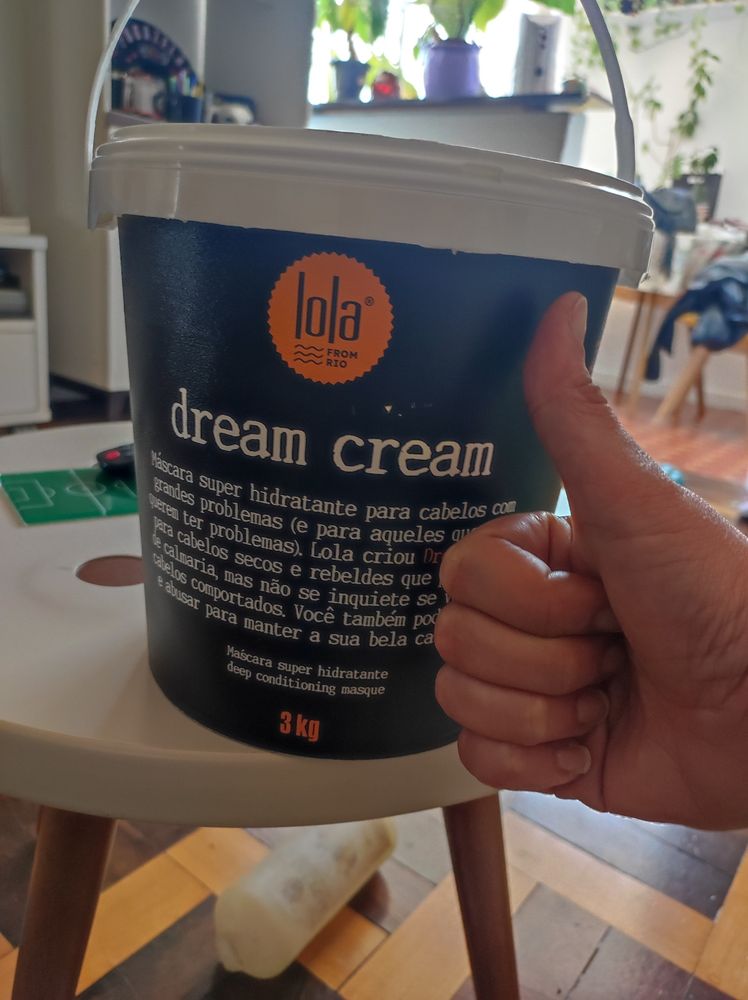 Um baldinho que tem 3kg de creme pra cabelo, da lola cosmeticos. O baldinho é preto e tem uma alcinha branca. Ao lado, minha mão fazendo joinha pra usar como escala (o baldinho fica maior que minha mão fazendo joinha)