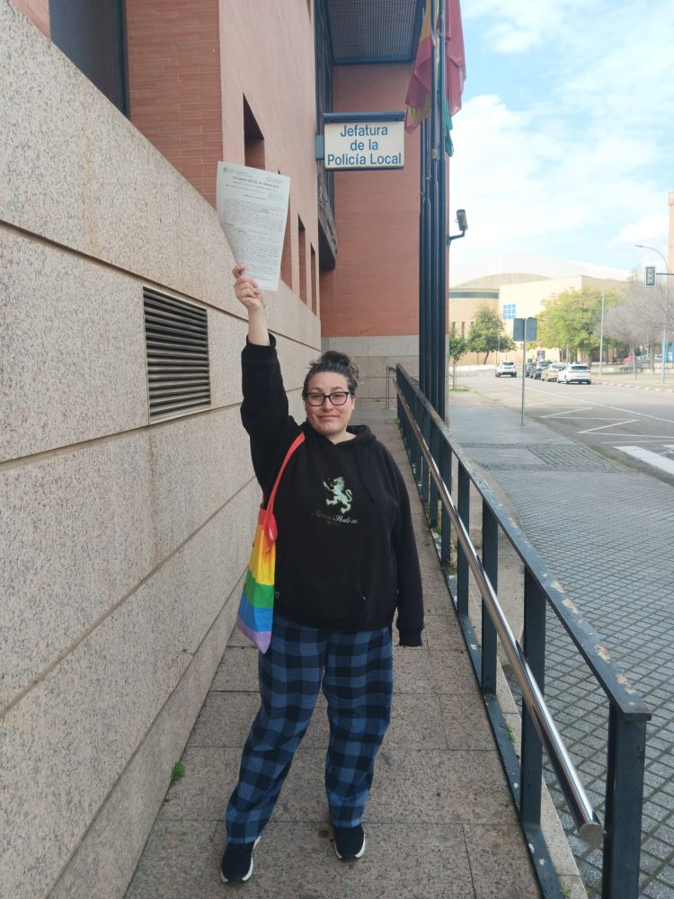 Yo a las puertas de la comisaría de Policía Local de Córdoba sosteniendo en mi mano la denuncia interpuesta. Llevo una totebag de la bandera del colectivo LGTBQI+