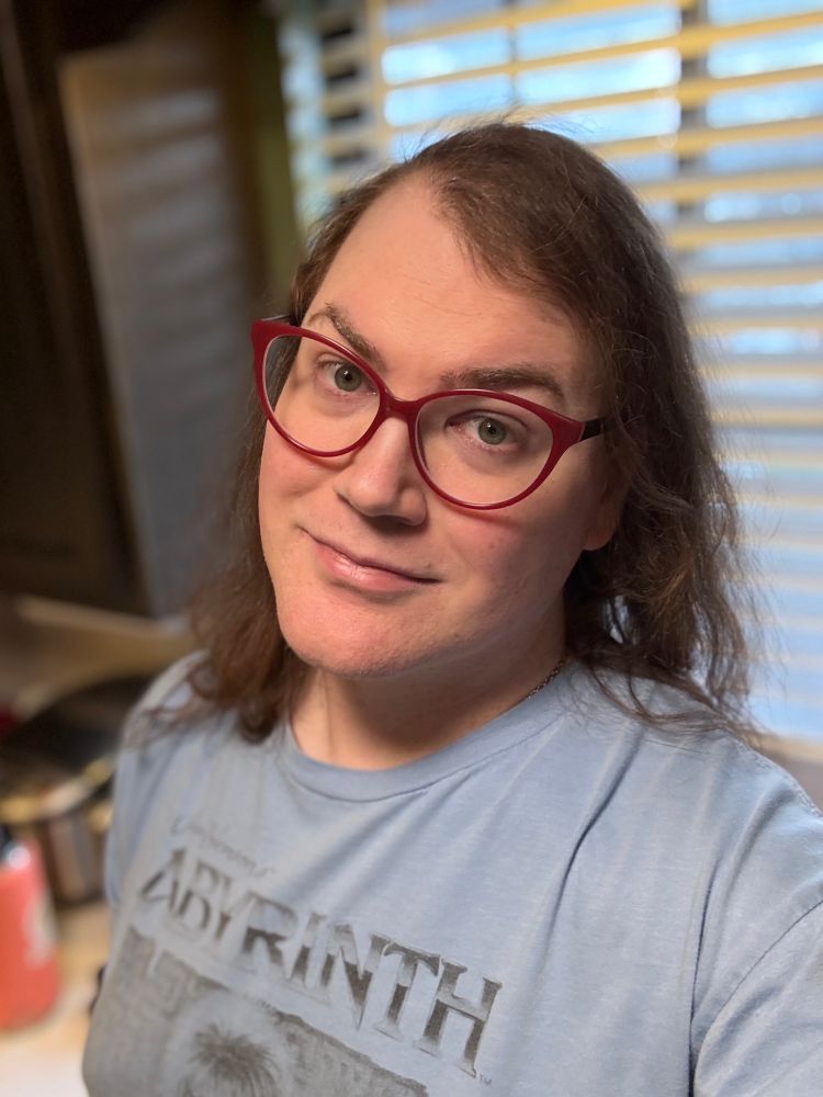 Lexi in a powder blue Labyrinth t-shirt and her red cat’s-eye frame glasses, standing in her kitchen.