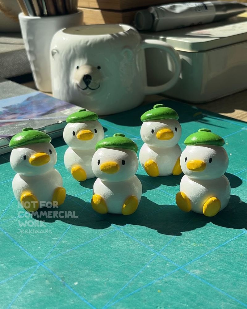 Photo showing 5 small white ducks made out of polymer clay, the ducks are sitting down and all are wearing green berets.