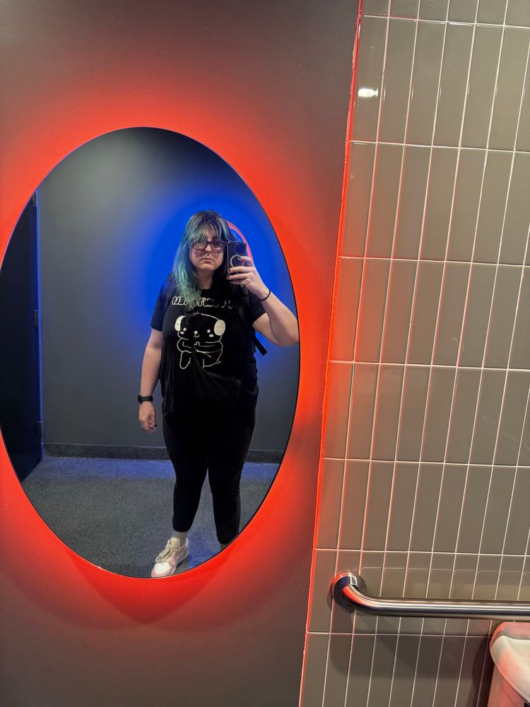 Lady in black taking selfie in bathroom with mirror backlit with red