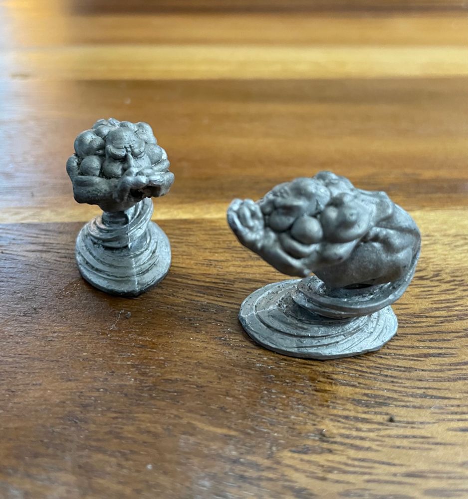 The same miniatures out of the packaging. They look like buff old bald guys with tornadoes for legs. They’re holding their hands up to their mouths as if to direct their wind breath forward.