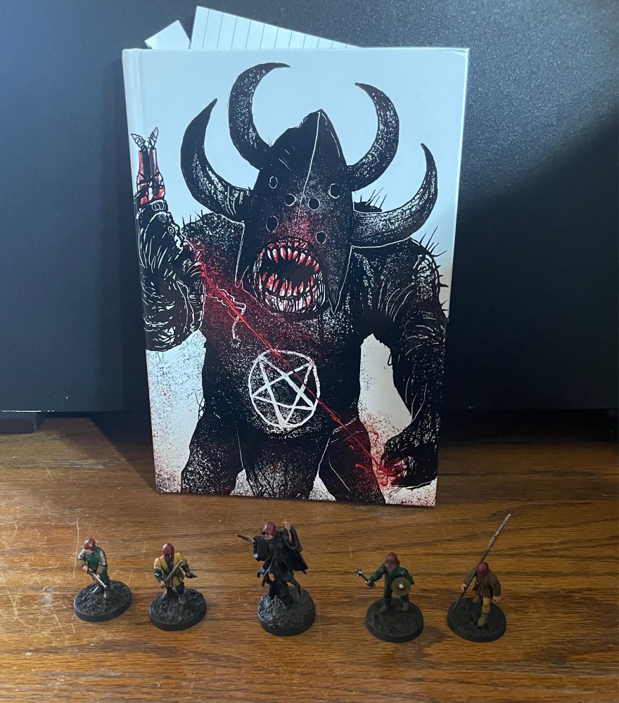 A warband of five 28mm gaming miniatures—a wizard and four soldiers—standing on a table in front of the Forbidden Psalm rule book.