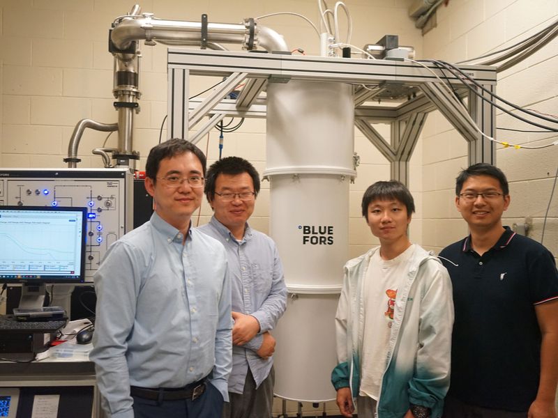 Four team members stand inside the lab around large white pipe and laptop.