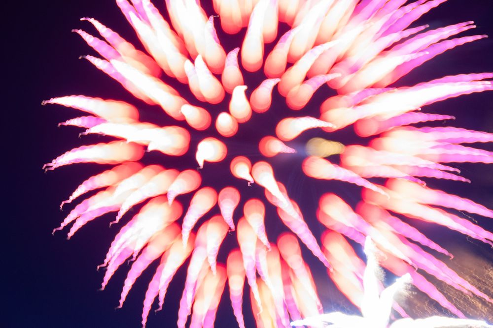 Bright spiky long-exposure firework with orange spikes and purple tips against a dark blue and purple sky.