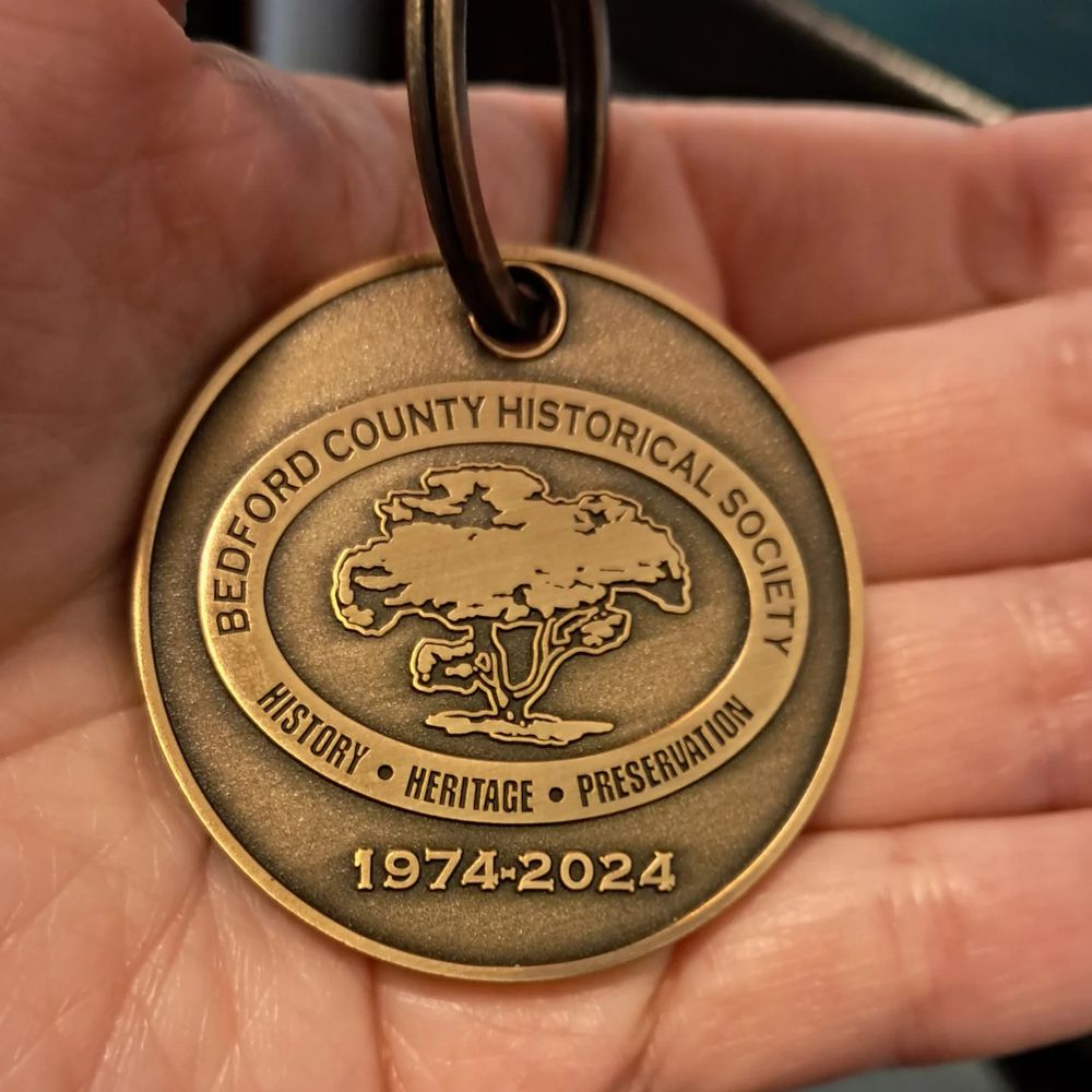 A commemorative medal on a key ring.  Picture is the front of the medal which shows a tree surrounded by an ellipical  on which the words Bedford County Historical Society,  History, Heritage, and Preservation are written. Below that is the text 1974-2024
