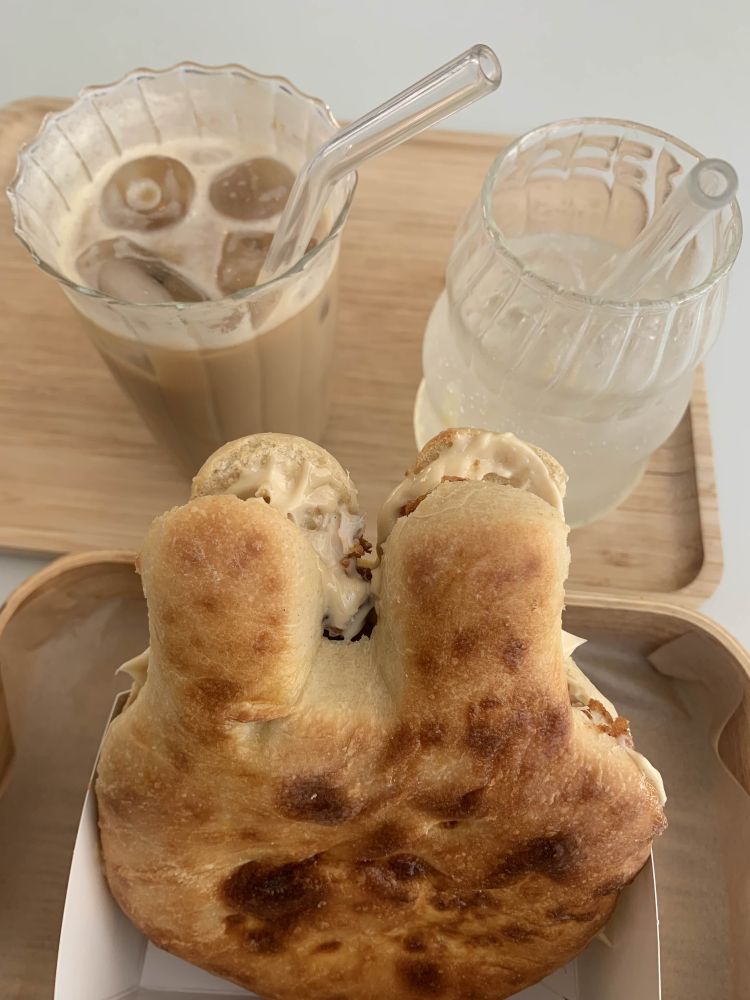 On the left, a banana iced latte with soy milk. On the right, a homemade sparkle lemonade. In the middle, a soft baked bread in the shape of a bunny, with teriyaki chicken, cheddar and a sweet homemade mayonnaise in it