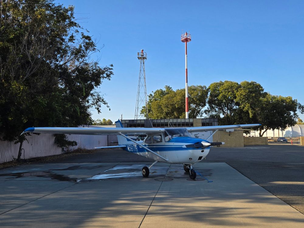 A blue and white Cessna 172 in the shade just after washing with old rotating beacons in the background