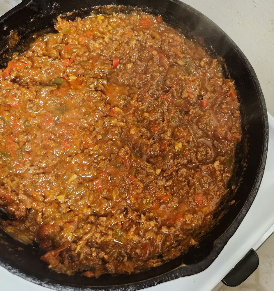 Cast iron skillet with simmering ground beef blended with the peppers, onions, and tomato sauce.