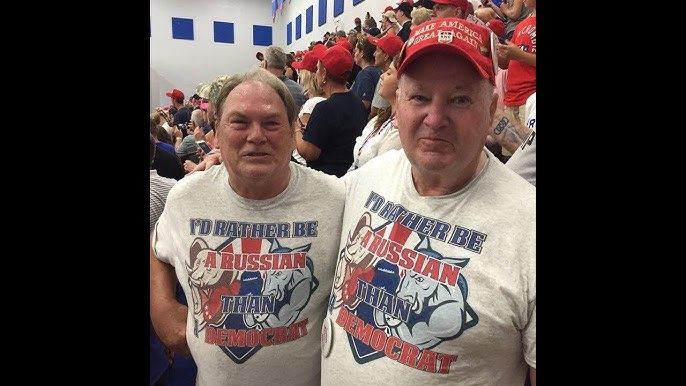 Two chubby white people, both male, with a T-Shirt which says: I'd rather be a russian than a democrat. One of them wears a read maga head.