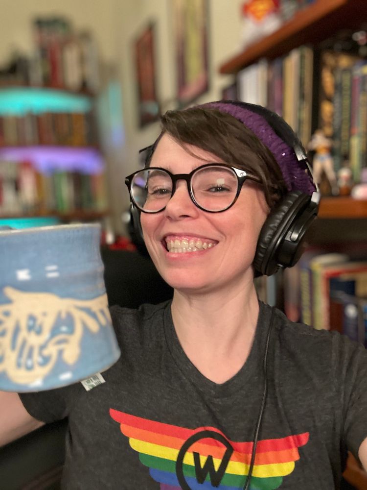 Smiling woman with headphones smiles and lifts a large mug. 