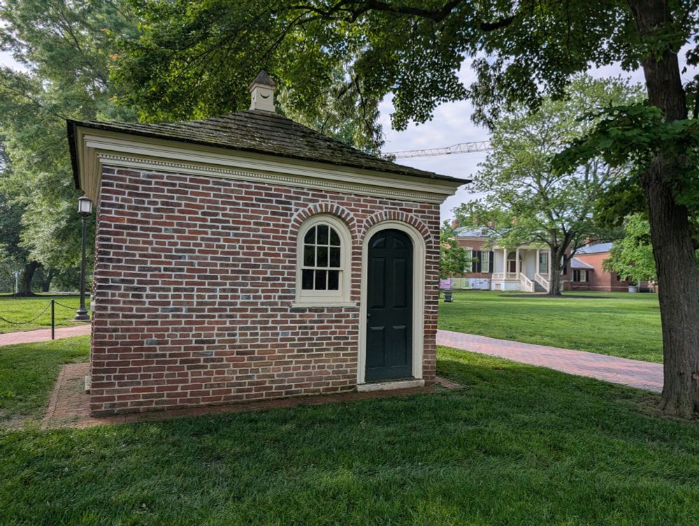 A brick shithouse on a leafy green lawn with an early 19th Century  mansion in the background