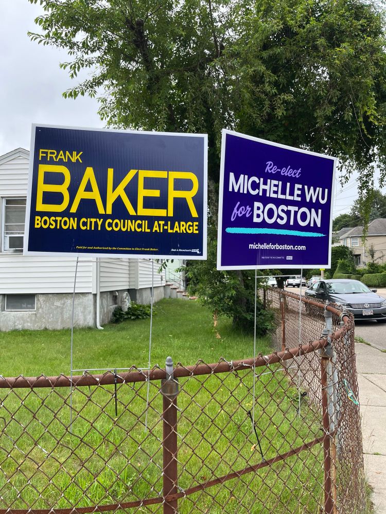 A Frank Baker for City Council and Michelle Wu for Mayor sign on a fence in fromt of a home.