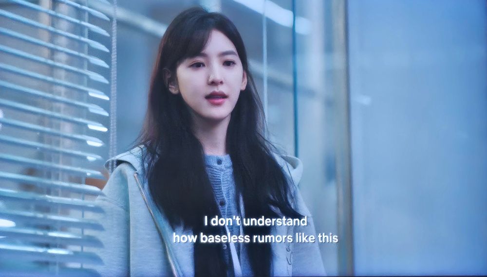 Wen Yifan says, "I don't understand how baseless rumors like this..." She wears a gray sweatshirt with a hoodie over a black shirt and blue shirt. She looks downward. This is from The First Frost, a cdrama.