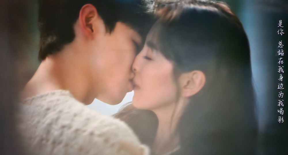 Sang Yan and Wen Yifan kiss as they embrace each other in their kitchen. He wears a white sweater and she a black one. This is from the cdrama The First Frost.