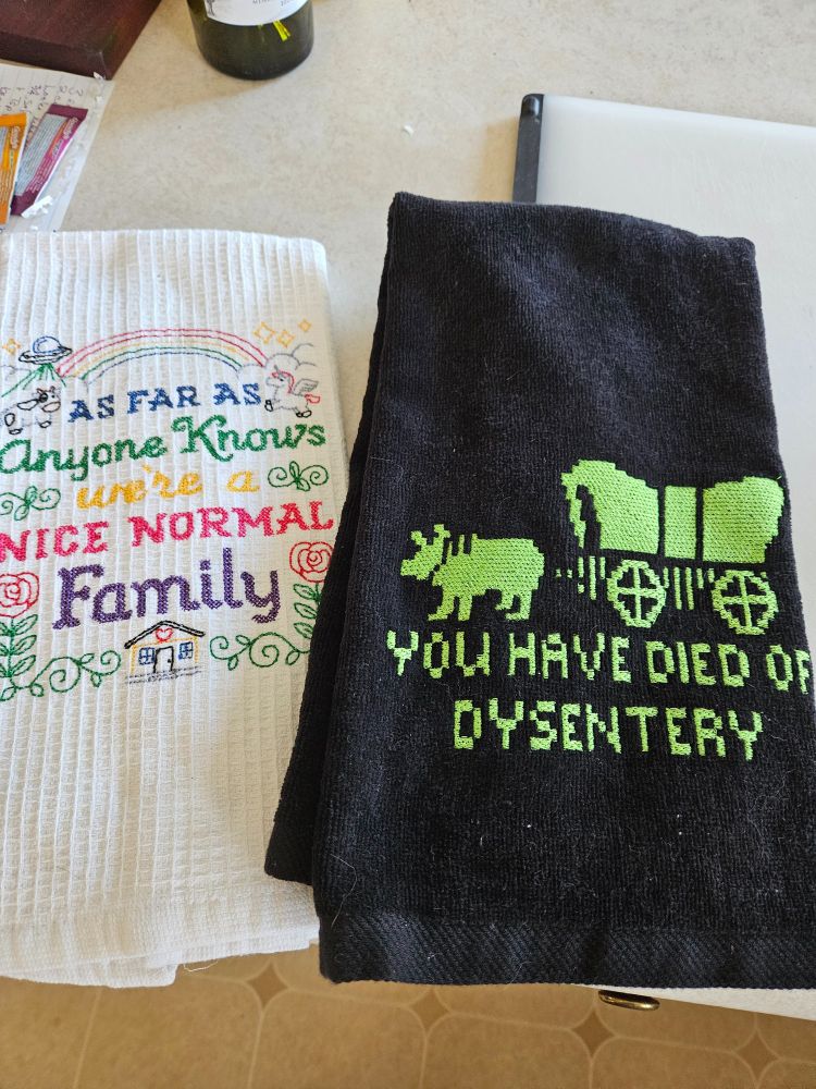 Black towel with the phrase "you have dies of dysentery" plus a pic of the wagon team from the DOS game Oregon Trail

White towel with the phrase "as far as anyone knows, we're a nice normal family"