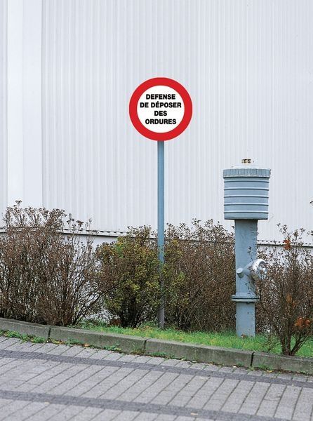 Dans une rue, un panneau blanc cerclé de rouge indique : "Défense de déposer des ordures".