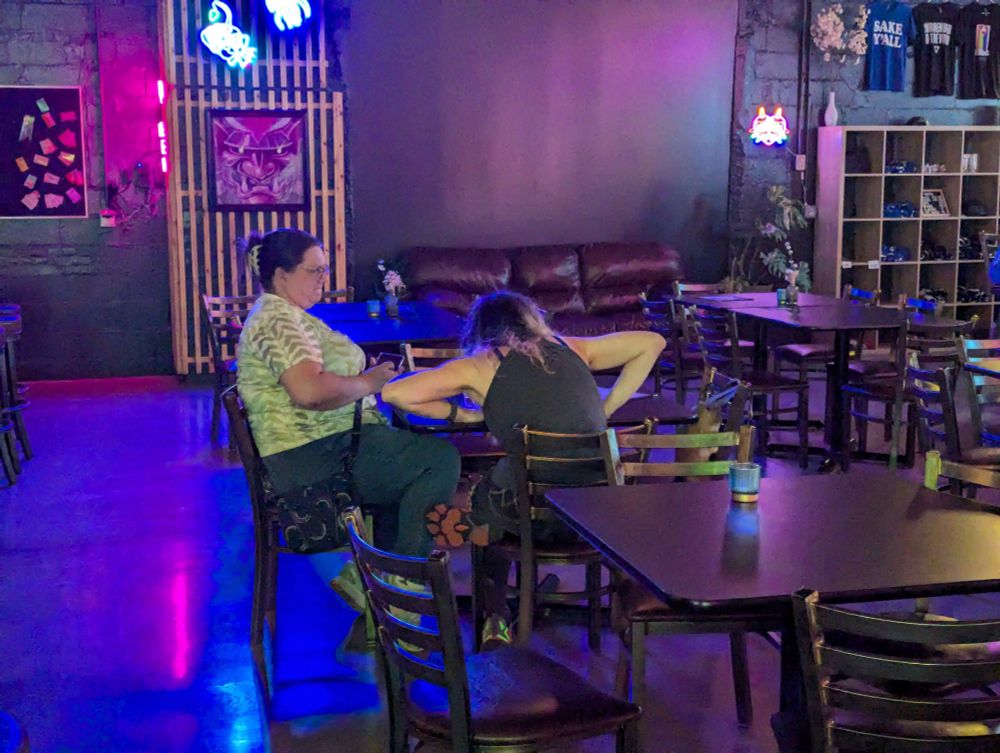 Some time after the other picture, returning to the table, viewed from a long distance, one of the idiotic queers (Mervyn) is still dramatically hunched over the table, staring intently at the drink. They are fully committed to The Bit.