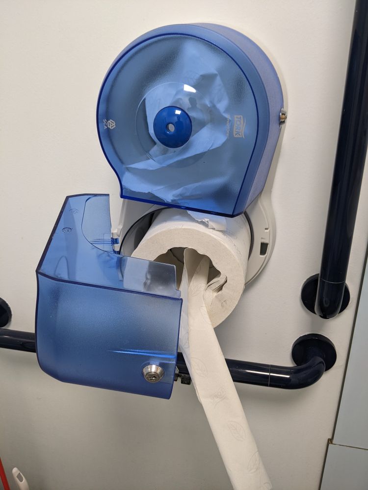 A photo of two blue toilet paper holders on a white wall. One of the holders has been unlocked and left open with the loo roll hanging freely. The other one, still closed as designed, has paper inside but no way to pull it out. 
