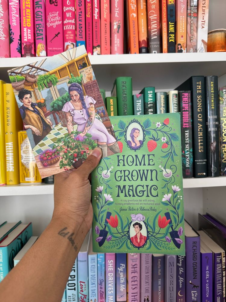 A hand holding Home Grown Magic by Jamie Pacton and Rebecca Podos and character art of the two main characters 