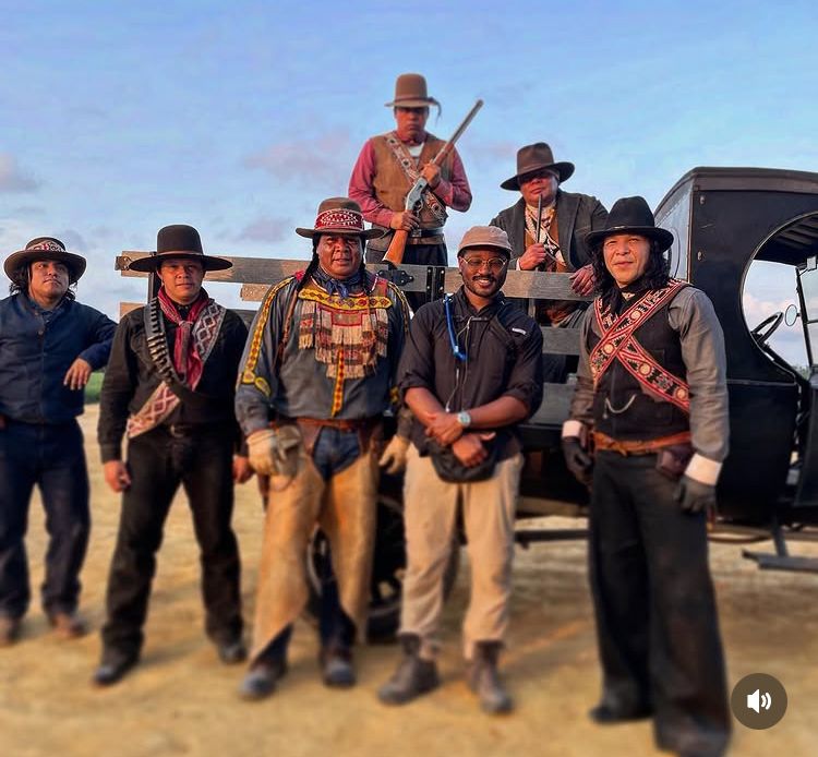 A set photo of Ryan Coogler and the actors who played the Choctaw vampire hunters in Sinners 
